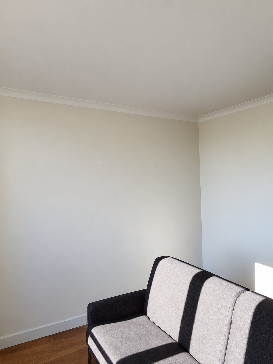 Un coin de pièce aux murs et au plafond fraîchement peints en blanc, avec un canapé noir et beige en bas à droite.