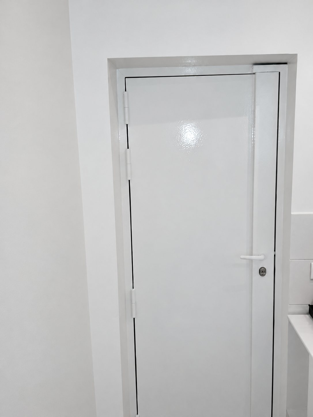 Une porte blanche brillante avec poignée et serrure, installée dans un encadrement au milieu de murs blancs.